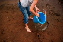 Chica de pie en la playa sosteniendo un cubo lleno de agua, Estados Unidos - foto de stock