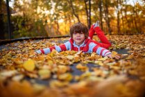 Портрет улыбающегося мальчика, лежащего на батуте, покрытом осенними листьями, США — стоковое фото