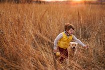 Boy and his dog running through a field at sunset, United States — Fotografia de Stock