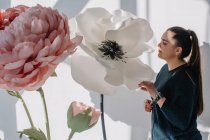 Портрет жінки, що стоїть поруч з гігантськими штучними квітами — стокове фото