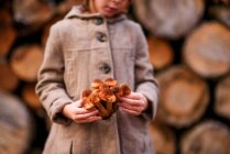 Girl Standing by a woodpile holding wild mushrooms, Estados Unidos - foto de stock