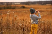 Niño de pie en un campo sosteniendo una hoja de hierba larga, Estados Unidos - foto de stock