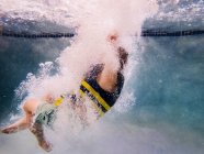 Vista subaquática de um menino pulando em uma piscina usando um colete salva-vidas — Fotografia de Stock