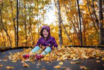 Smiling girl sitting on a stack of autumn leaves on a trampoline, United States — Stock Photo