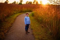 Niño parado en un sendero junto a un campo al atardecer, Estados Unidos - foto de stock