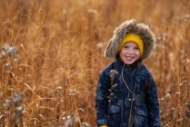 Retrato de una niña sonriente de pie en un campo masticando un pedazo de hierba larga, Estados Unidos - foto de stock