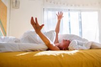 Junge liegt mit erhobenen Armen im Bett — Stockfoto