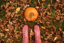 Overhead view of a woman feet standing next to a pumpkin — Stock Photo