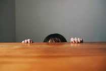 Девушка прячется за столом, обрезанный образ — стоковое фото