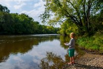 Boy standing on a riverbank fishing, United States — Stock Photo