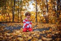 Lächelnder Junge sitzt auf einem Trampolin, das mit Herbstblättern bedeckt ist, Vereinigte Staaten — Stockfoto