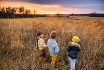 Trois enfants debout dans un champ au coucher du soleil, États-Unis — Photo de stock