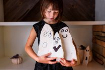 Menina sorridente segurando três decorações fantasmas de madeira para o Halloween — Fotografia de Stock