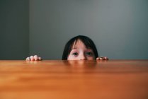 Mädchen versteckt sich hinter einem Tisch — Stockfoto