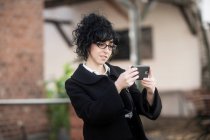 Женщина, стоящая на улице, фотографируется со своим мобильным телефоном, Германия — стоковое фото