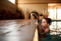 Menina segurando a borda de uma piscina — Fotografia de Stock