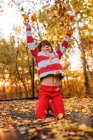 Мальчик на коленях на батуте бросает осенние листья в воздух, США — стоковое фото