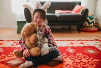 Smiling girl wearing bunny ears sitting on the floor with soft toys — Stock Photo