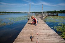 Хлопчик сидить на пристані, приманюючи приманку до свого риболовецького стрижня, Сполучені Штати Америки. — стокове фото