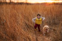 Ragazzo che insegue il suo cane attraverso un campo al tramonto, Stati Uniti — Foto stock