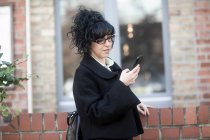 Улыбающаяся женщина стоит на улице, используя свой мобильный телефон, Германия — стоковое фото
