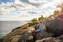 Boy sitting on rocks by a lake, Lake Superior Provincial Park, Stati Uniti — Foto stock