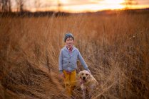 Boy standing in a field with his golden retriever dog, United States - foto de stock
