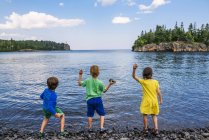 Tres niños lanzando piedras a un lago, Split Rock Lighthouse State Park, Minnesota, Estados Unidos - foto de stock