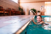 Smiling Girl holding on to the edge of a swimming pool — Stock Photo