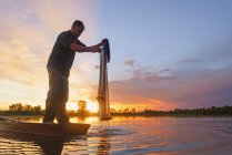 Silhouette eines Fischers, der bei Sonnenuntergang in einem Boot mit einem Fischernetz steht, Thailand — Stockfoto