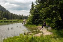 Mulher sentada junto a um lago treelined no verão, Bulgária — Fotografia de Stock