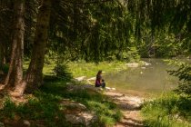 Mujer sentada junto a un lago arbolado en verano, Bulgaria - foto de stock