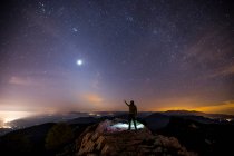 Vue arrière d'un homme debout sur une montagne la nuit pointant vers le ciel, Mare De Deu Del Mont, La Garrotxa, Gérone, Catalogne, Espagne — Photo de stock