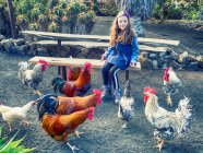 Ragazza sorridente seduta su una panchina che nutre un gruppo di galli e una gallina, Lanzarote, Isole Canarie, Spagna — Foto stock
