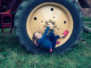 Chica sonriente sentada en una gran rueda tractor en una granja, Polonia - foto de stock