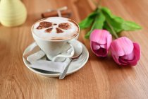 Two pink tulips next to a cup of coffee on a wooden table — Stock Photo