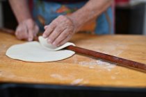 Крупним планом руки старшої жінки розкачують тісто на дошці — стокове фото