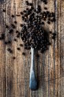 Черный перец в деревянной ложке на деревенском фоне — стоковое фото