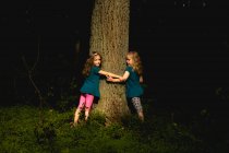 Duas meninas de pé em um jardim à noite abraçando uma árvore, Polônia — Fotografia de Stock