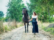 Belle femme conduisant un cheval le long d'une route de campagne, Pologne — Photo de stock