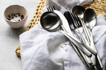Stack of cutlery on a napkin and place mat with a bowl of salt and pepper — Stock Photo