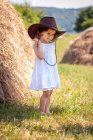 Menina vestindo um chapéu de cowboy em pé em um campo por um fardo de feno, Bulgária — Fotografia de Stock