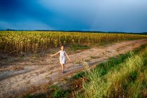 Ragazza che cammina lungo il bordo di un campo di girasole con le braccia tese, Ungheria — Foto stock