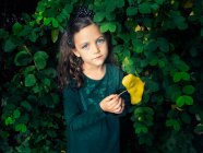 Chica de pie junto a un arbusto sosteniendo una hoja, Italia - foto de stock