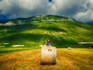 Ragazza seduta su una balla di fieno in un campo, Castelluccio di Norcia, Umbria, Italia — Foto stock