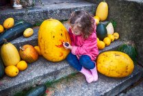 Girl sitting on a step drawing a smiley face on a Halloween pumpkin, Poland — Stock Photo