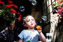 Girl standing outside a house blowing soap bubbles, Poland — Stock Photo