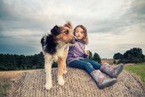 Menina sentada em um fardo de feno ao lado de seu cão, Polônia — Fotografia de Stock