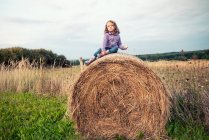 Девушка сидит на тюке сена в поле, Польша — стоковое фото