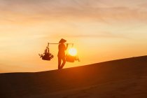 Donna che trasporta cestini attraverso una duna di sabbia al tramonto, Mui Ne, Vietnam — Foto stock